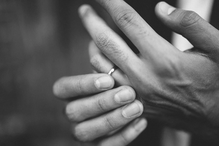 Photo en noir et blanc de deux mains, l’une portant une alliance fine à l’annulaire