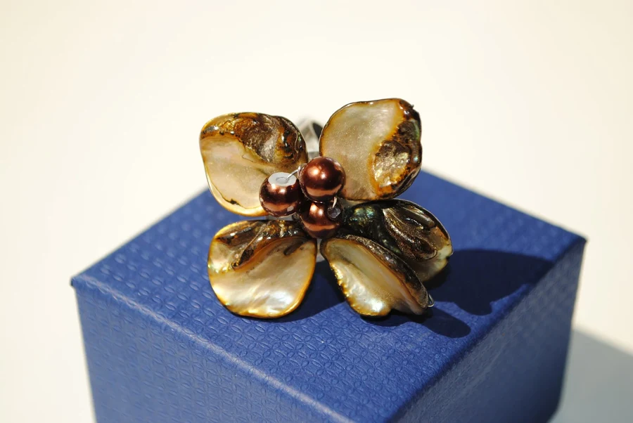 Bague ornée d’une perle de Tahiti brune et de nacre en forme de fleur, posée sur un coffret bleu